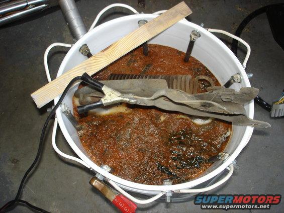 Bucket with rusty water, metal parts, and jumper cables for electrolysis rust removal