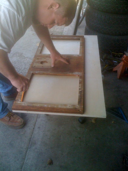 Man marking a wooden frame with a pencil, resting on a larger board