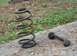 1976 Ford Ranchero - Two automotive suspension components, a rusty coil spring and a sway bar end link, are displayed on a concrete surface.
