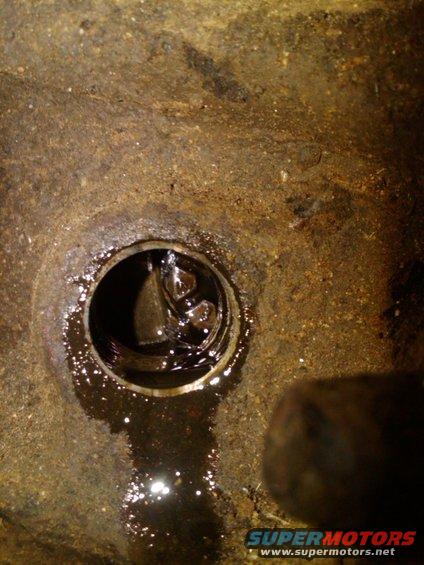 Close-up of an engine oil drain plug with oil around it