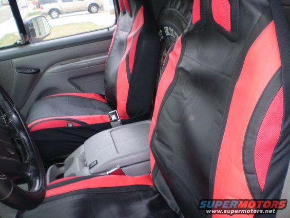 Interior view of a vehicle showing front seats with black and red custom seat covers and a center console