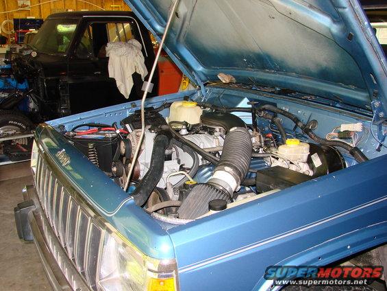 Blue Jeep Comanche with hood open, showing engine. Black truck in background