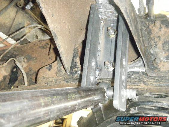Close-up of custom suspension bracket and linkage on a vehicle's undercarriage. Some text is visible on a metal tube