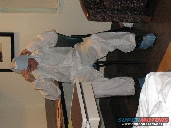 Person wearing a white disposable suit and blue booties sits with head in hands