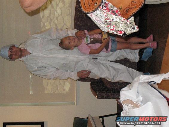 Man in a white protective suit holding a young girl. She is wearing a pink shirt and denim shorts