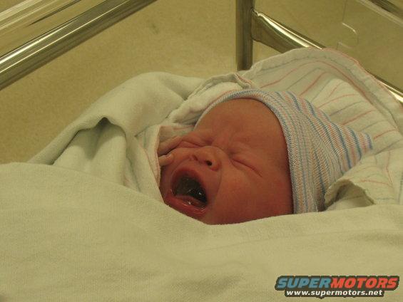 Newborn baby wrapped in a blanket and wearing a hospital hat, crying