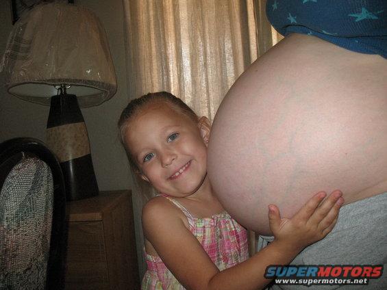 Young girl hugs a large pregnant belly. Supermotors logo in corner