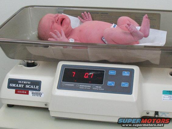 Newborn baby crying on a digital scale showing 7.07