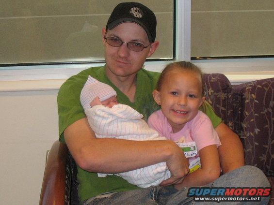 Man holding a newborn, with a young girl smiling next to him