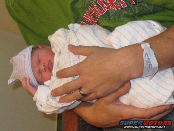 Newborn baby in a hospital hat and blanket, held by an adult with a hospital wristband