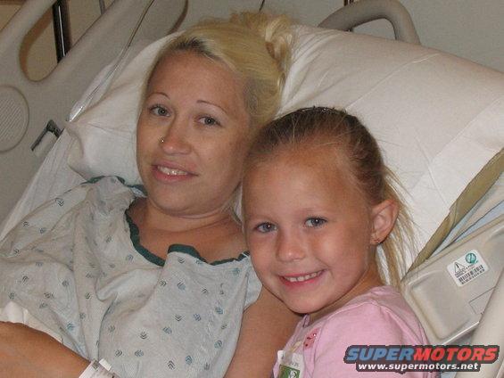 Woman and young girl smiling in hospital beds, wearing hospital gowns and a pink shirt