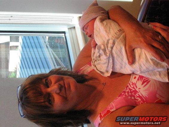 Woman holding a newborn baby, with Supermotors.net logo visible