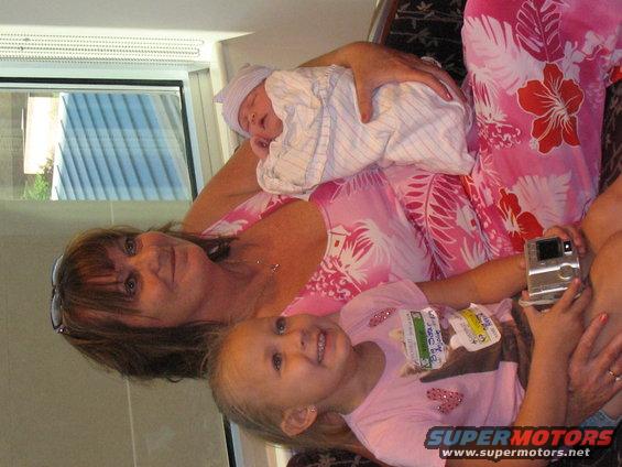 Woman holding a baby and a young child. The child has a camera