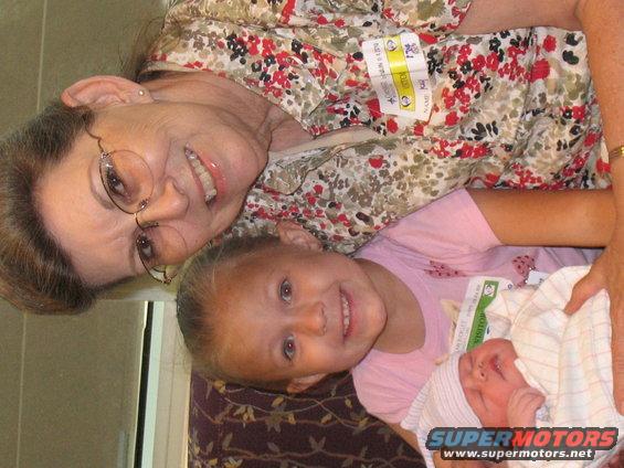 Three people, an adult woman, a young girl, and a newborn baby, with visitor badges visible