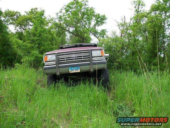 Front view of a red pickup truck with a brush guard, driving through tall grass and trees