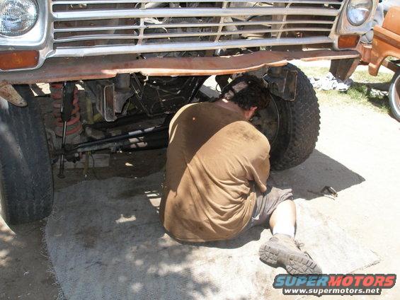 Man working on the front wheel of a truck, under the grille and bumper