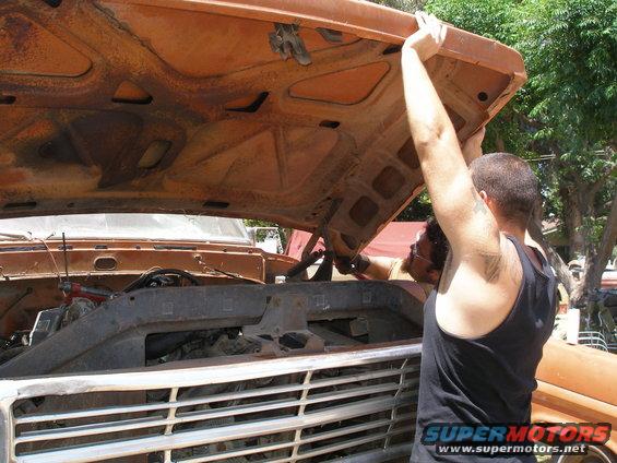 Two men lifting the hood of an orange 1970s Ford truck to access the engine bay