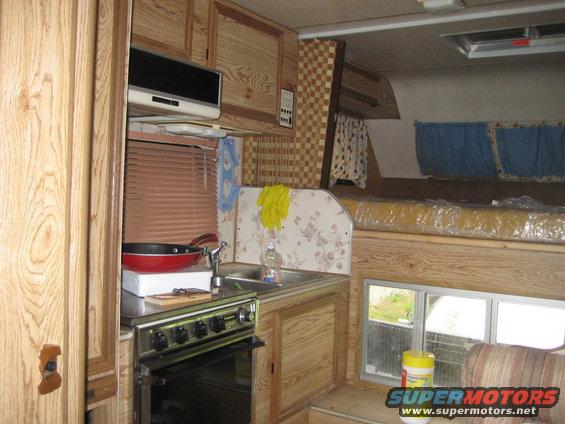Camper interior with kitchenette, sink, stove, and bed