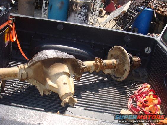 Rear axle assembly with differential housing and brake drum, secured with orange straps in a truck bed