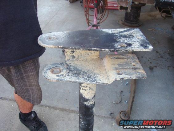 Dirty metal bracket assembly with bolt holes, held by a black pipe