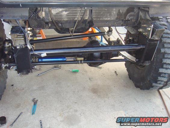 Vehicle undercarriage with large tires, suspension linkages, and a blue steering stabilizer