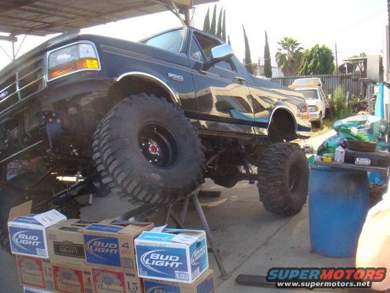 Lifted black Ford Bronco on stands, with boxes of Bud Light in front. Another vehicle is parked in the background