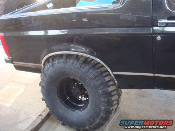 Black SUV's large off-road tire and fender flare. Chrome trim along the body