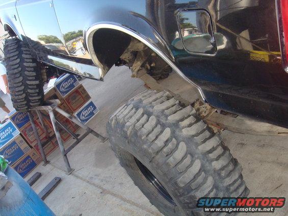 Black SUV rear fender and large off-road tire, supported by stands and Bud Light cases