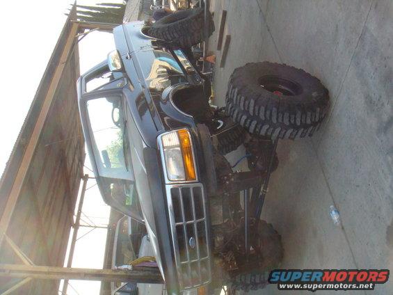 Black Ford truck with large off-road tires, lifted suspension, and custom grille