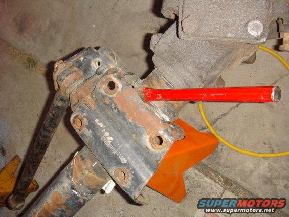 rusted metal axle component held by orange jack stand, red chisel inserted