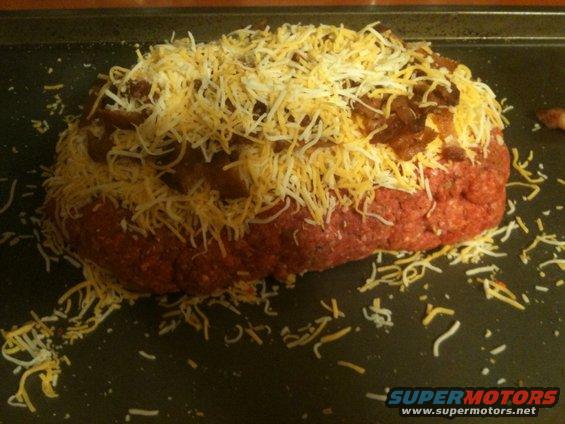 Meatloaf topped with shredded cheese and crumbled bacon on a baking sheet
