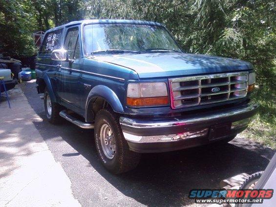 Blue Ford Bronco parked on asphalt driveway, trees in background