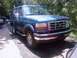 1995 Ford Bronco - This blue Ford Bronco is parked outdoors on a paved surface with trees behind it.