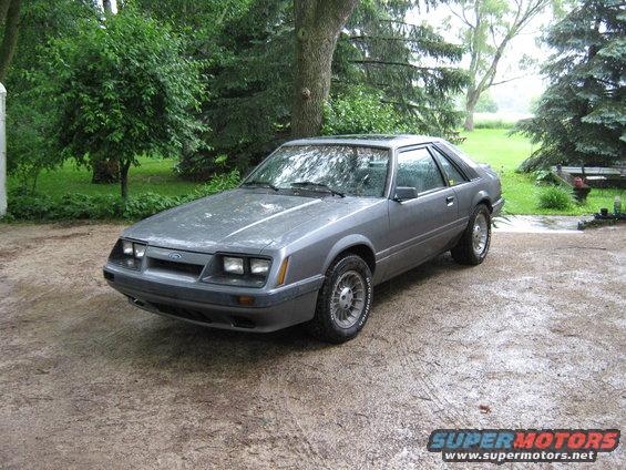Gray coupe parked on a gravel driveway with trees and grass in the background