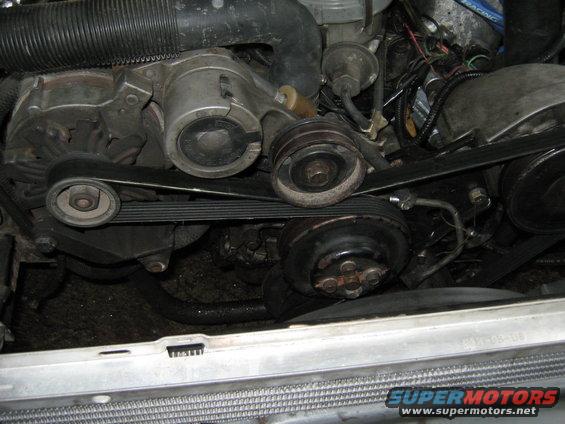 Engine bay with belts, pulleys, and hoses visible. Some dirt and grime present