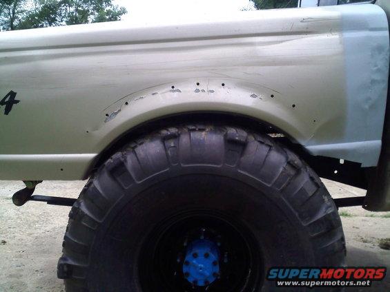 Side view of a truck bed with large tires and visible rust around the wheel well