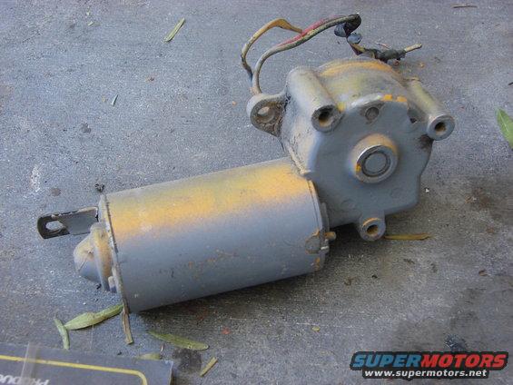 Gray electric motor with yellow paint splatters and wires attached, lying on a concrete surface