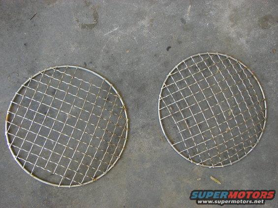 two round metal grilles with wire mesh, lying on a concrete surface