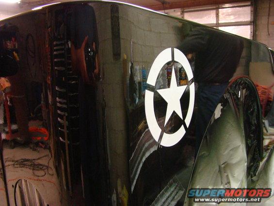 Close-up of a black Jeep fender with a white star-in-circle decal. Some green tape is visible on the lower right
