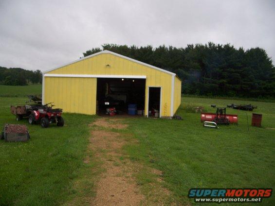 Yellow barn with ATV, trailer, and equipment in yard