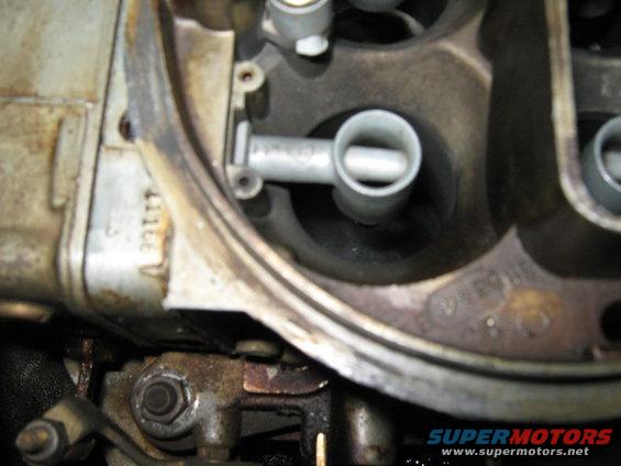 Close-up of carburetor interior with a metal tube extending into a chamber. Some numbers are visible on the side