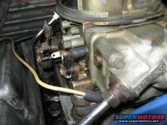 Close-up of a dirty carburetor with yellow and black wires, and metal linkages
