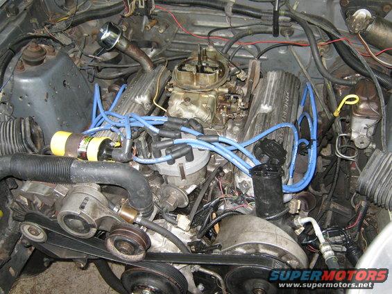 Engine bay with V8 engine, carburetor, blue spark plug wires, and distributor cap