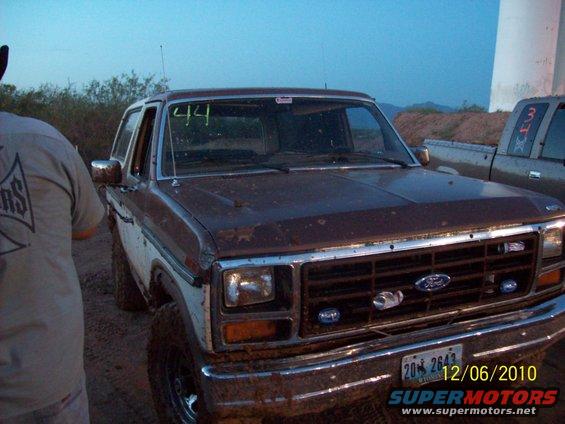 Brown and white 1985 Ford Bronco front view, muddy, with '44' written on windshield