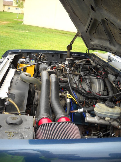 Engine bay with aftermarket air intake, yellow battery, and blue hoses. Hood is open