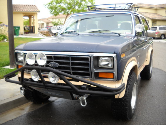 Blue Ford Bronco front view, aftermarket bumper with four lights, roof rack