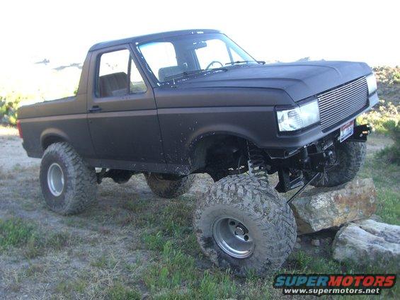 Black lifted Ford Bronco with large off-road tires on rocks, matte paint, chrome grille, visible suspension