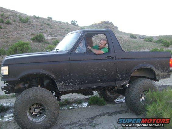 1987 Ford Bronco with lifted suspension and large tires driving off-road