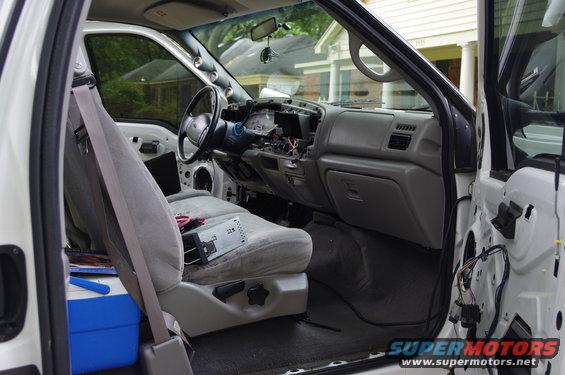Interior of a white 1999 Ford F-250 with dashboard disassembled, gray seats, and a blue cooler