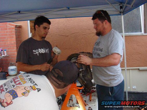 Three guys working on a differential assembly on an orange jack stand